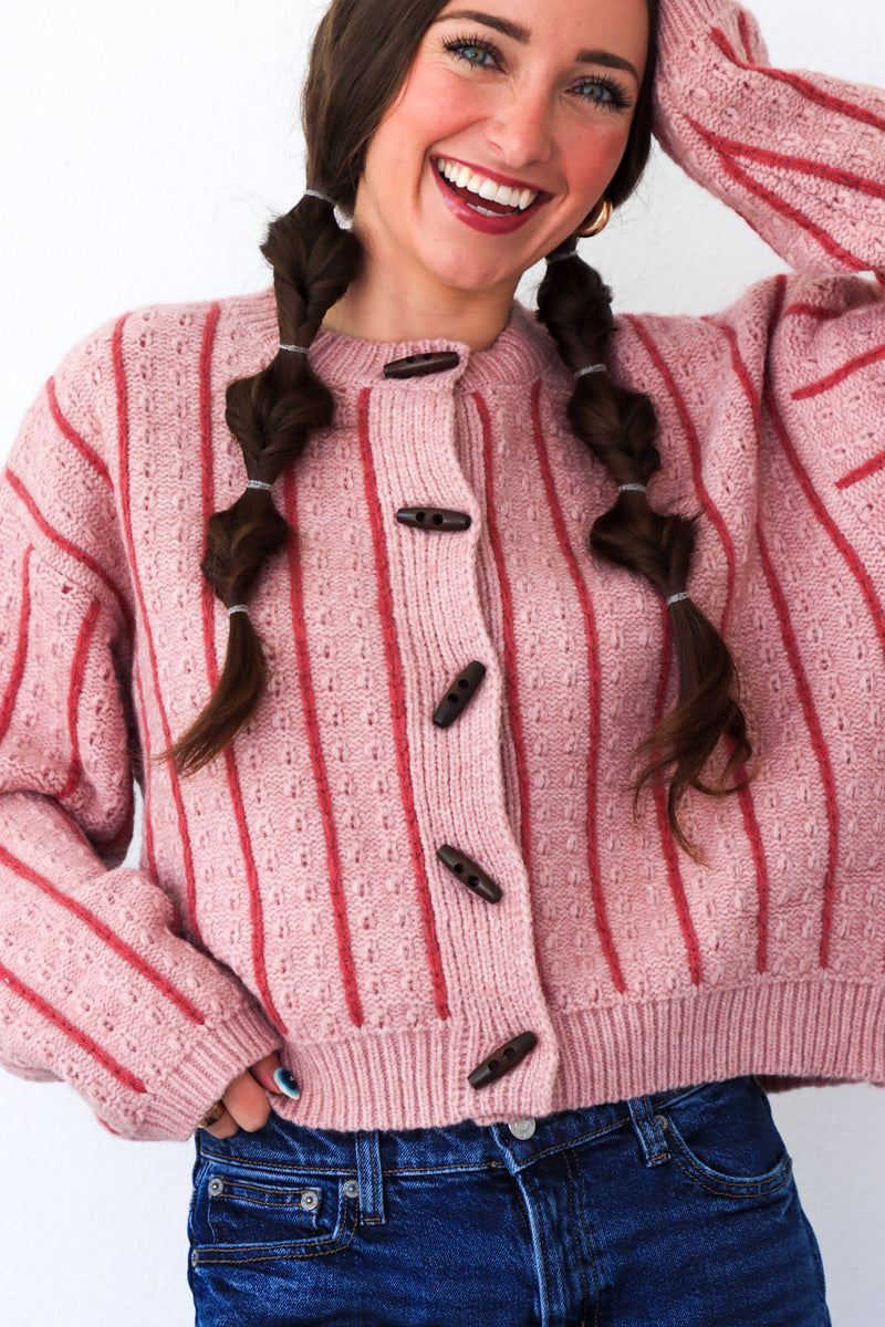Woman wearing a pink and red striped sweater with buttons, smiling against a white background