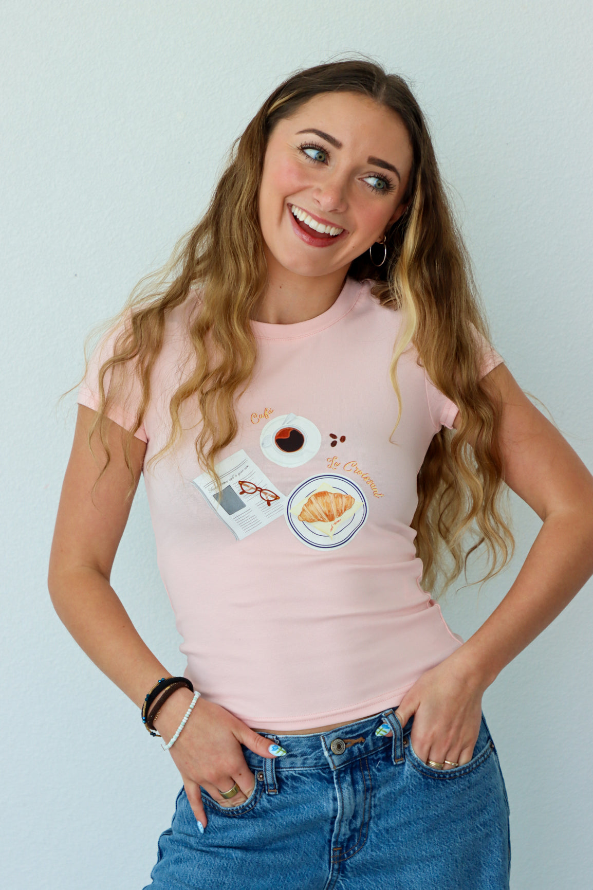 Woman wearing a pink t-shirt with graphics and text, standing against a light background