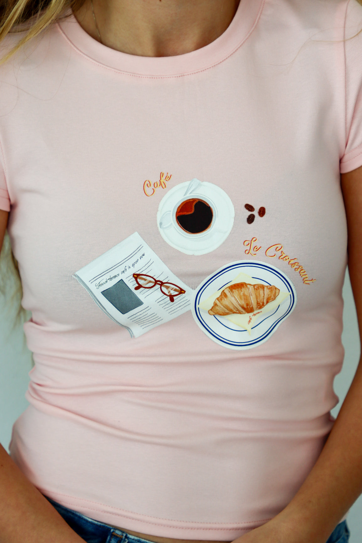 Pink t-shirt with coffee and croissant design worn by a person