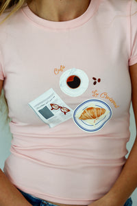 Pink t-shirt with coffee and croissant design worn by a person