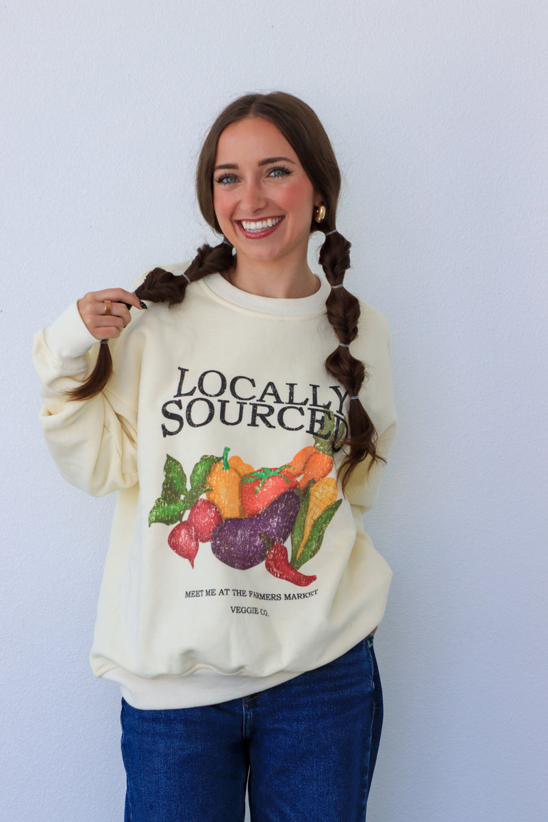 Woman wearing a cream-colored sweatshirt with a colorful graphic and text against a white background