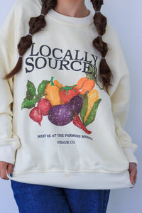 Woman wearing a cream-colored sweatshirt with 'Locally Sourced' graphic