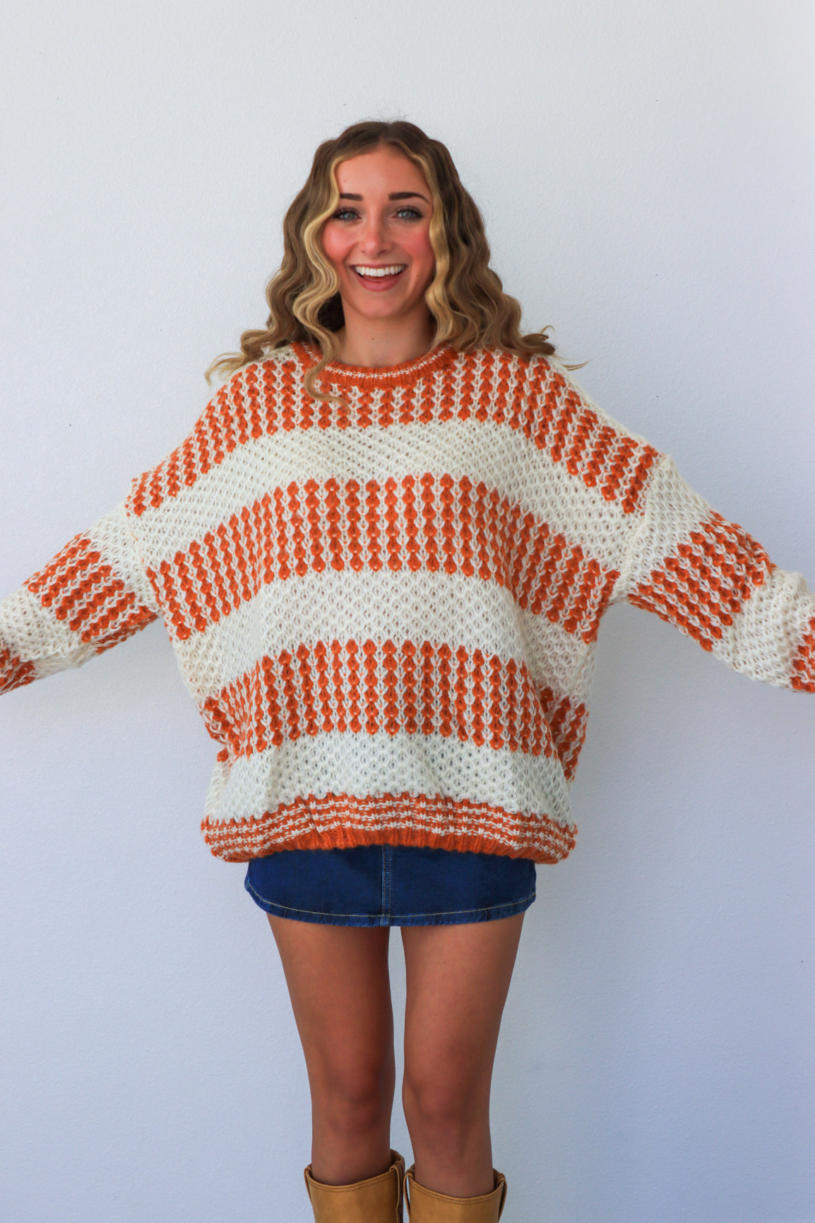 Woman wearing a large orange and white striped sweater on a plain background