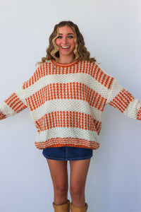 Woman wearing a large orange and white striped sweater on a plain background