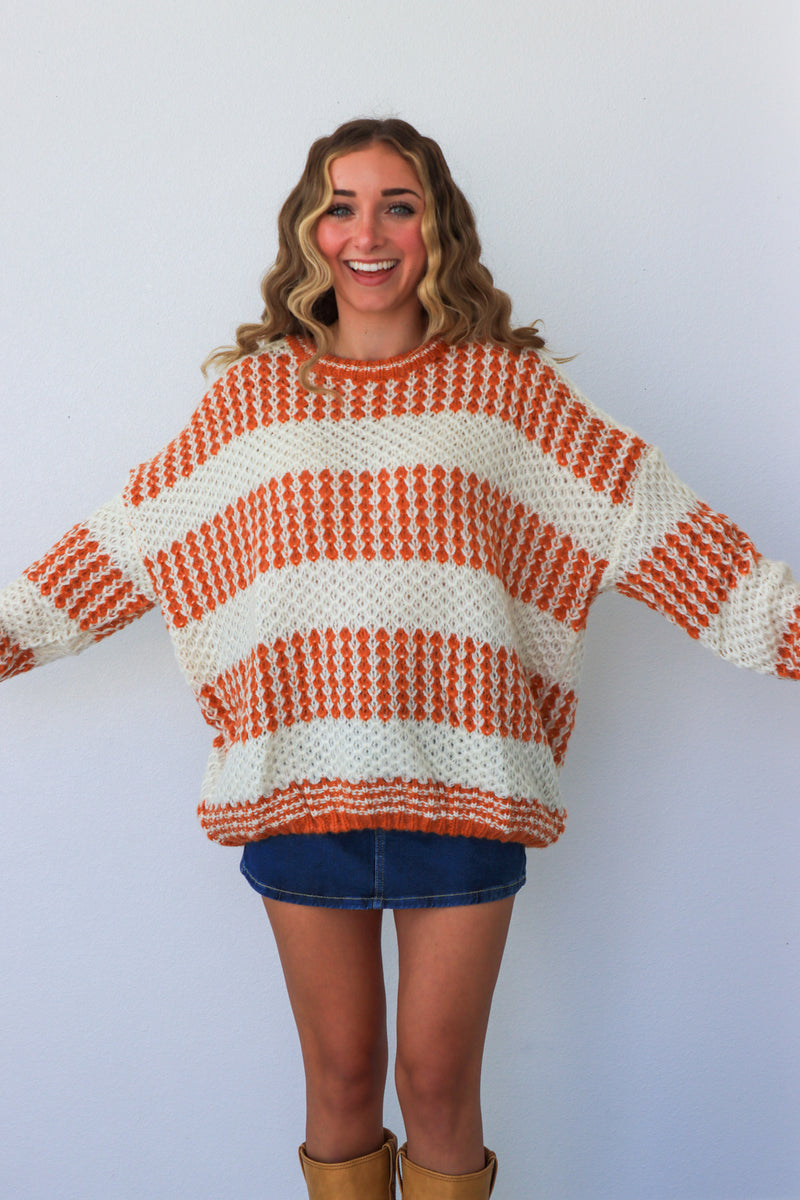 Woman wearing a large orange and white striped sweater on a plain background