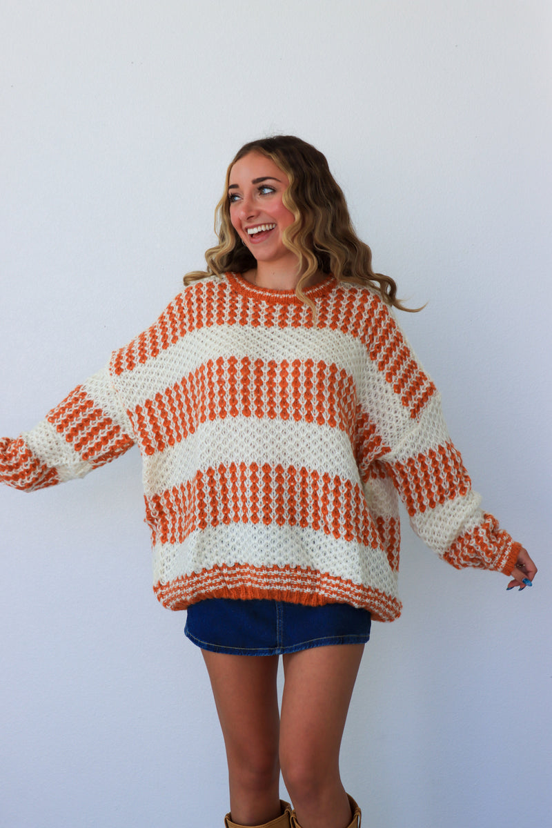 Woman wearing a large orange and white patterned sweater against a plain background