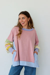 Woman wearing a pink shirt with colorful cuffs and hem against a white background