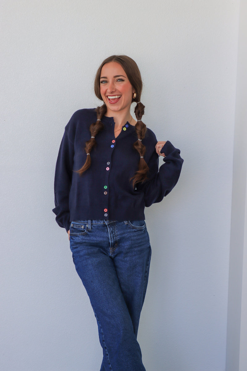 Woman wearing a navy blue shirt and jeans standing against a white wall.