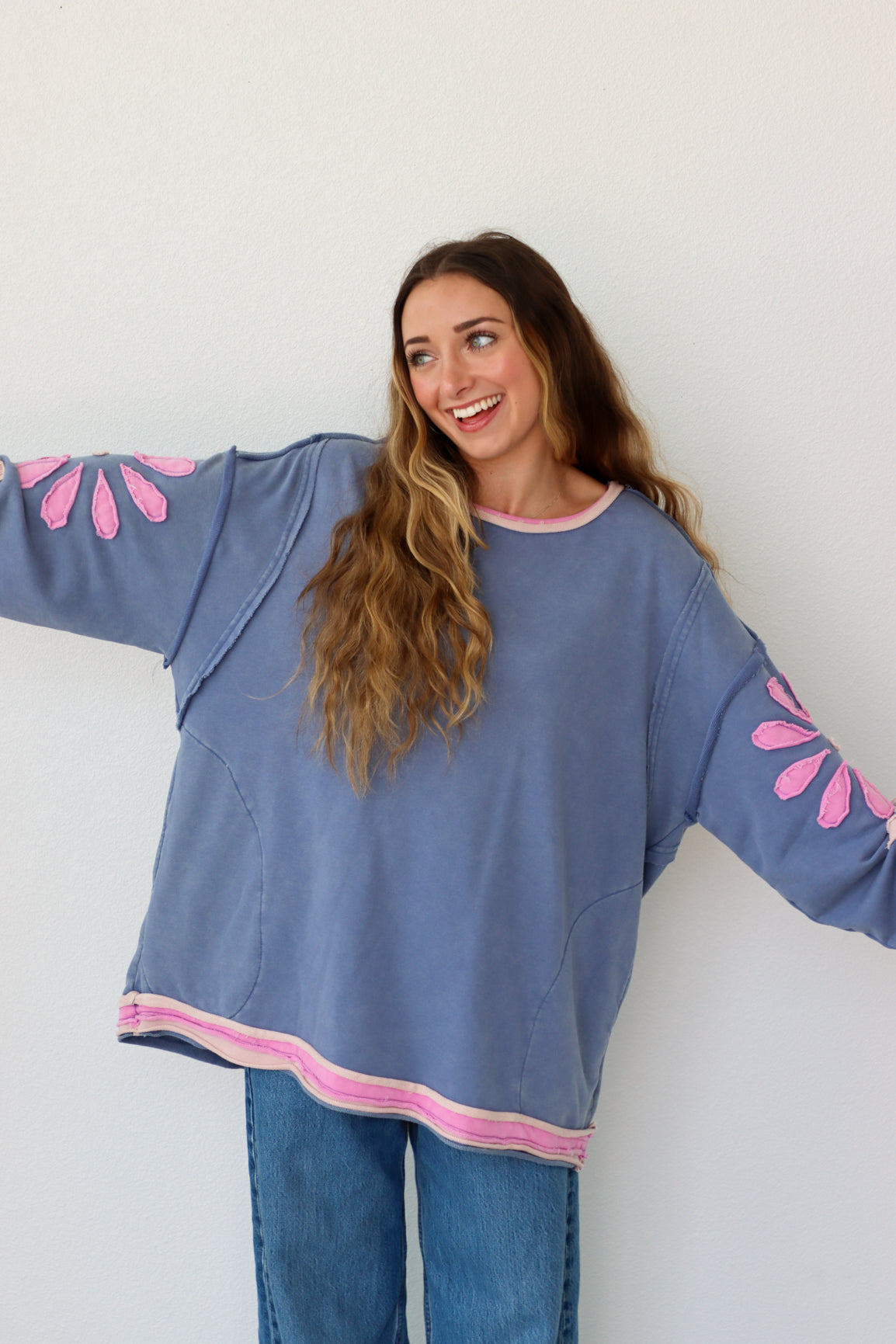 Woman wearing a blue shirt with pink floral patterns on sleeves against a white background