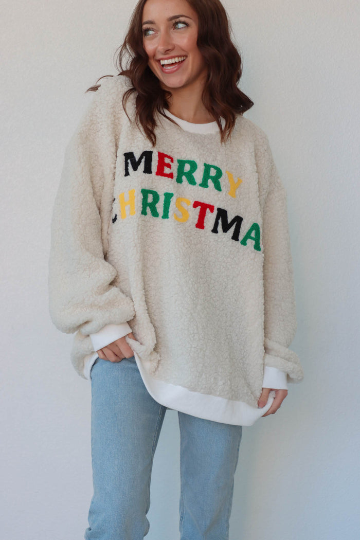 girl wearing cream sherpa crewneck with multicolor "Merry Christmas" patch lettering