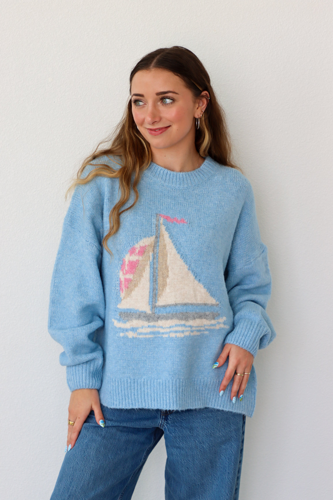 Woman wearing a blue sweater with a sailboat design against a white background