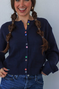 Woman wearing a navy blue cardigan with colorful buttons against a plain background