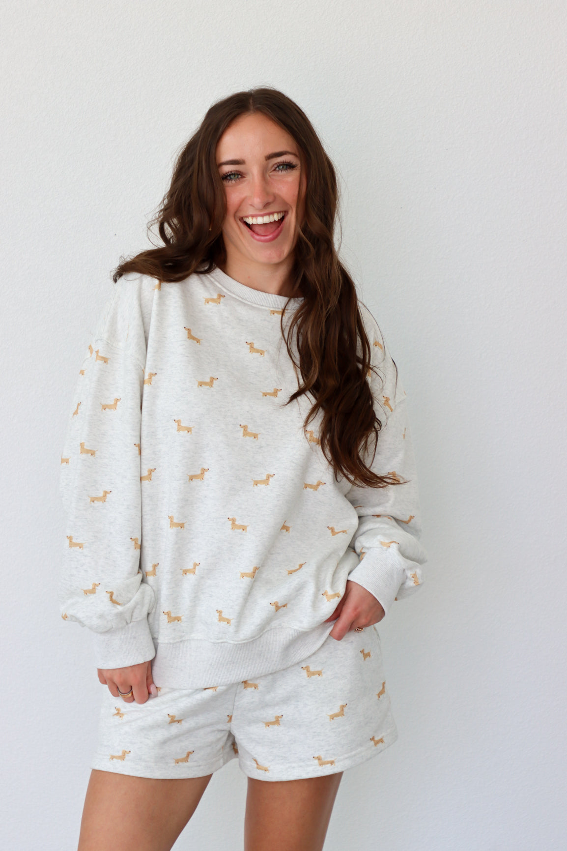 Woman wearing a gray sweatshirt and shorts set with small patterns, laughing against a plain background