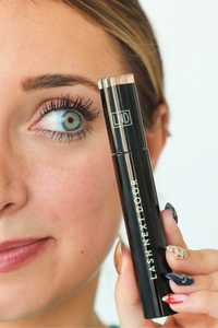 Woman holding a black eyelash product with 'LND' branding.