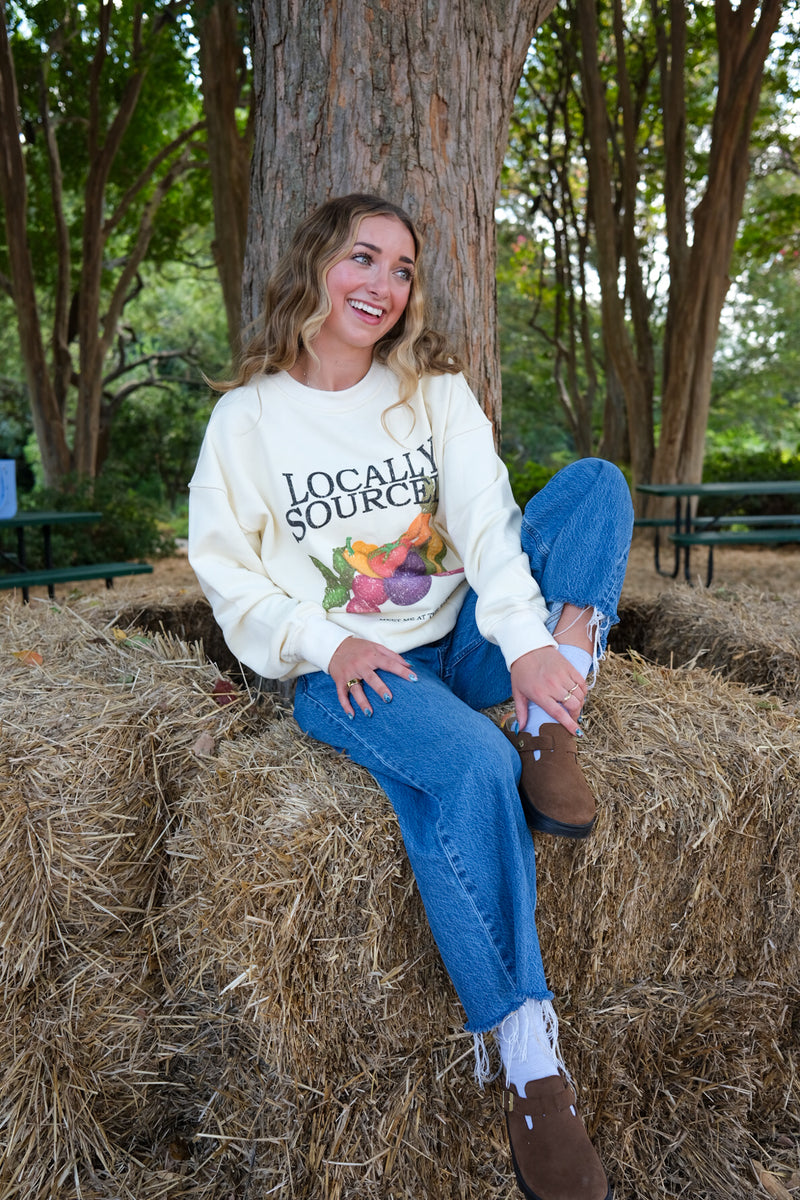 Woman wearing a cream-colored sweatshirt with 'Locally Sourced' graphic