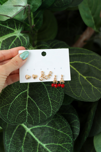 Set of gold and red earrings on a card held against green leaves