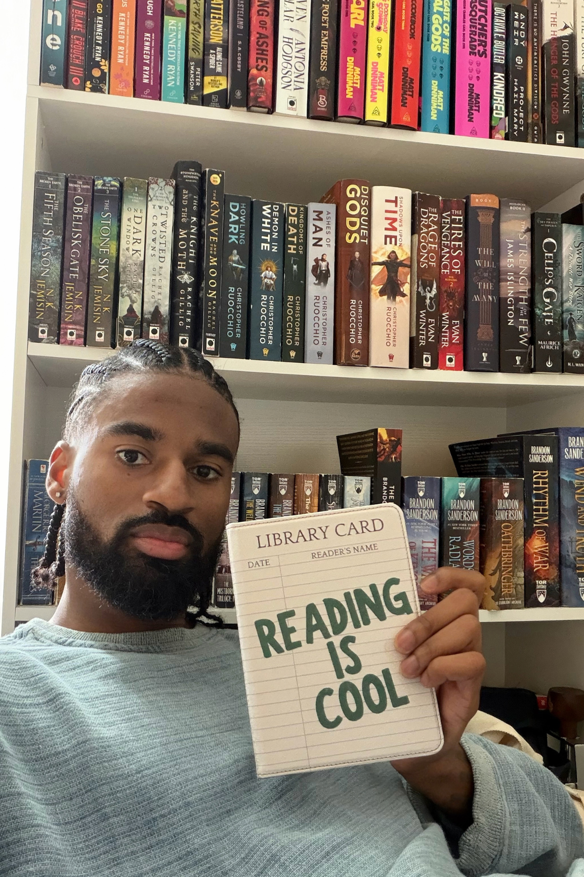 A man holding a Kindle Case that says "Reading is Cool" in front of a library of books 