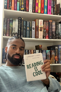 A man holding a Kindle Case that says "Reading is Cool" in front of a library of books 