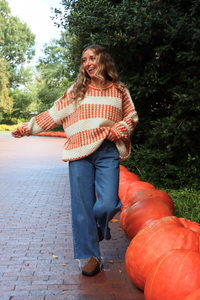 Woman in a colorful sweater standing next to pumpkins outdoors