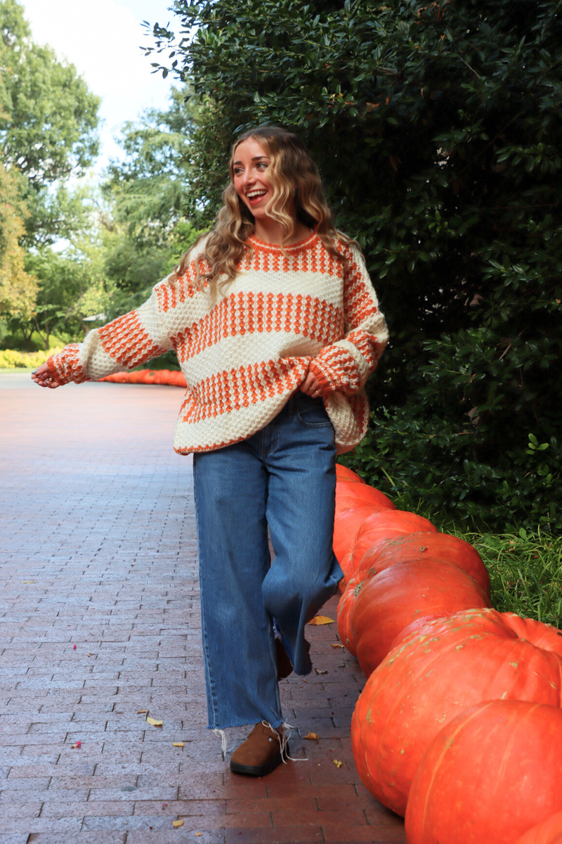 Woman in a colorful sweater standing next to pumpkins outdoors