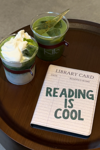 Two matcha green tea drinks in clear cups with a kindle case that says 'READING IS COOL' in green text.