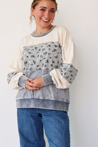 Woman wearing a color-blocked sweater with floral patterns on a plain background