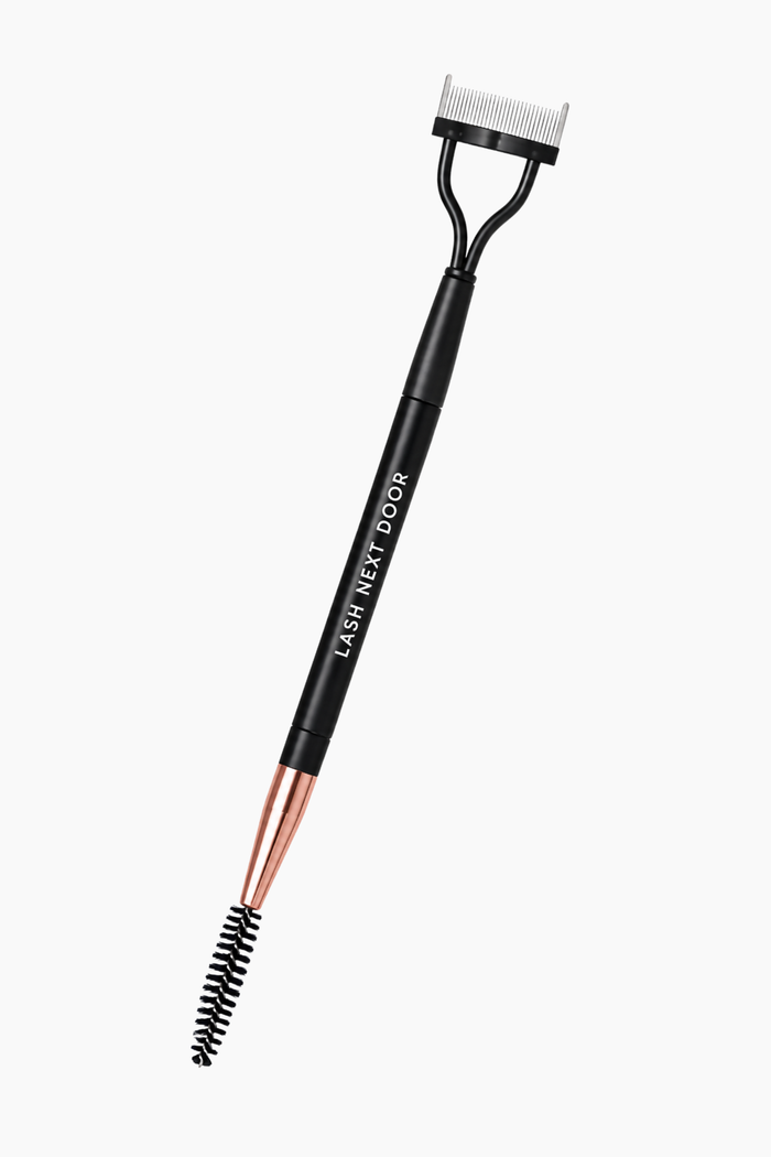 A black eyelash net tool with rose gold metal accents and a white bristle comb, shown on a plain light gray background.