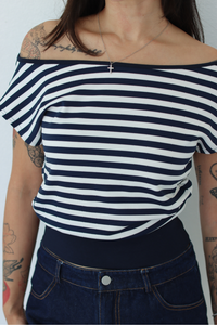 A woman wearing a navy and white horizontally striped off-the-shoulder top with a wide navy waistband, paired with dark blue jeans.