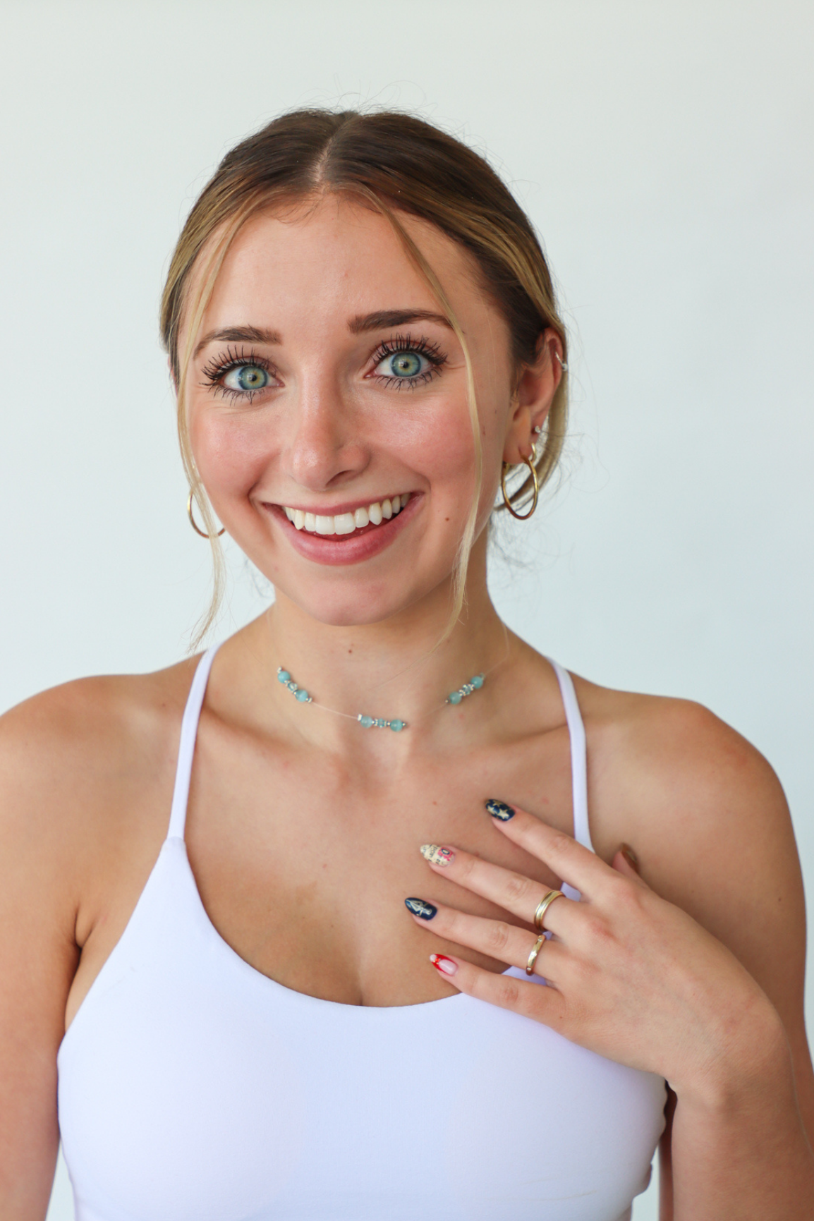 Woman wearing a white tank top with jewelry on a plain background