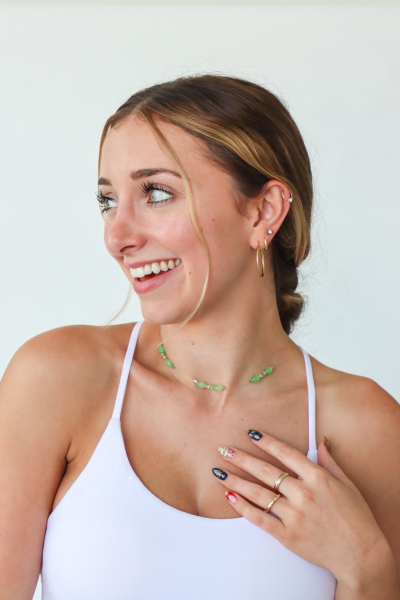 Woman wearing a white tank top with a necklace and earrings against a plain background
