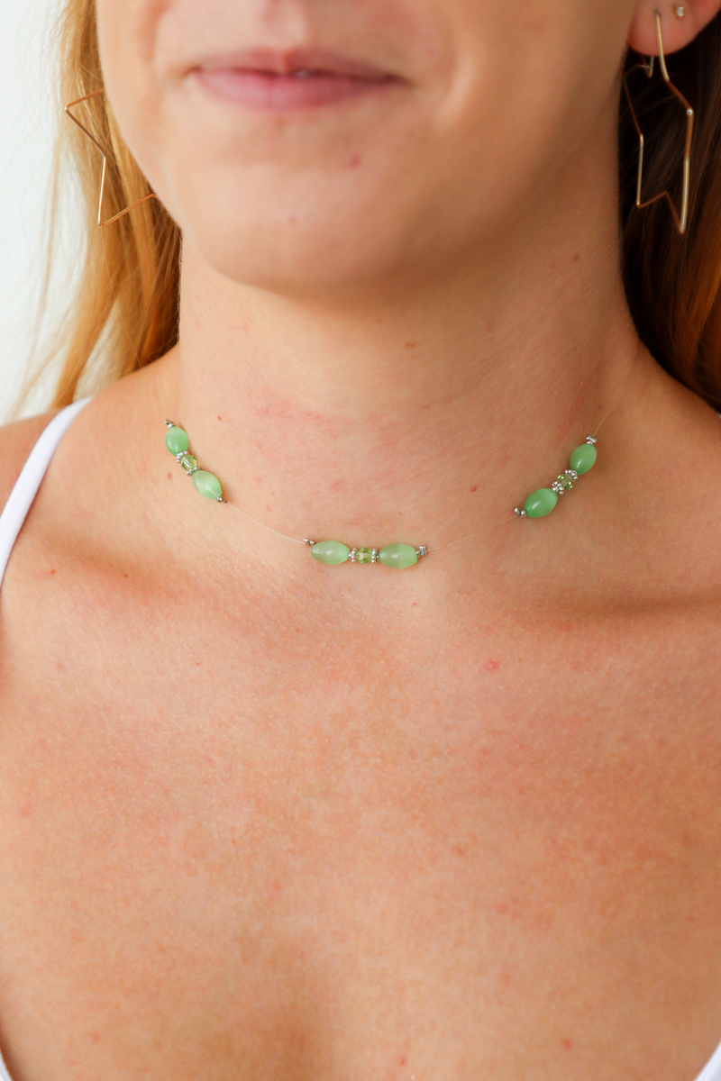 Close-up of a person wearing a green beaded necklace with matching earrings.