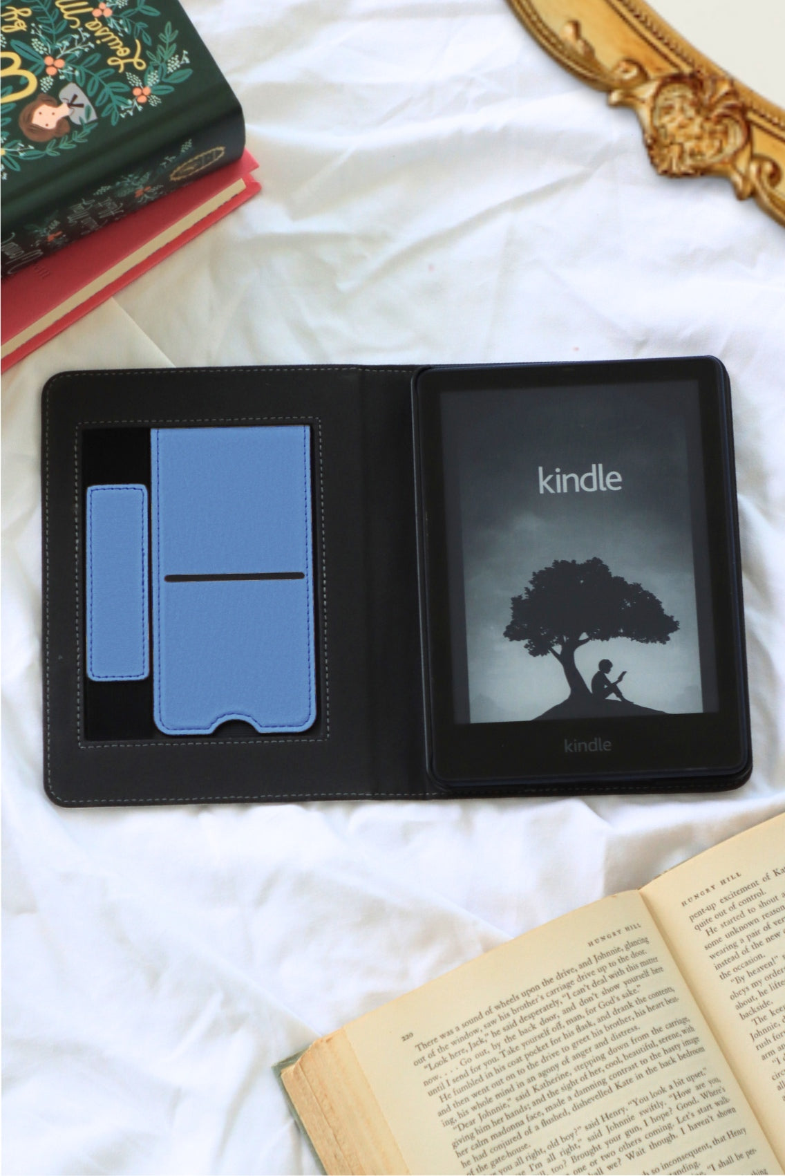 Kindle device with a black case on a white surface with books around