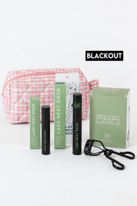Lash Next Door eyelash extension kit with a pink and white gingham cosmetic bag, black mascara tubes, a green product box, and a black strap, displayed on a white background with a 'BLACKOUT' label.