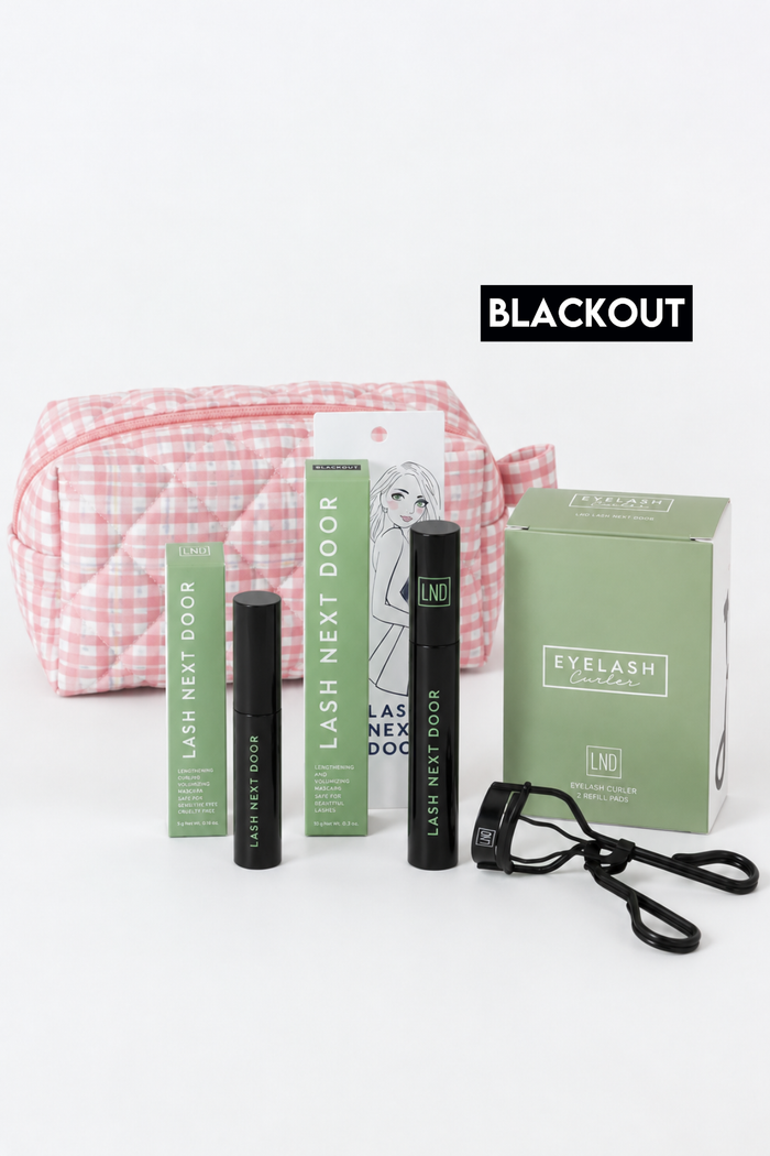 Lash Next Door eyelash extension kit with a pink and white gingham cosmetic bag, black mascara tubes, a green product box, and a black strap, displayed on a white background with a 'BLACKOUT' label.