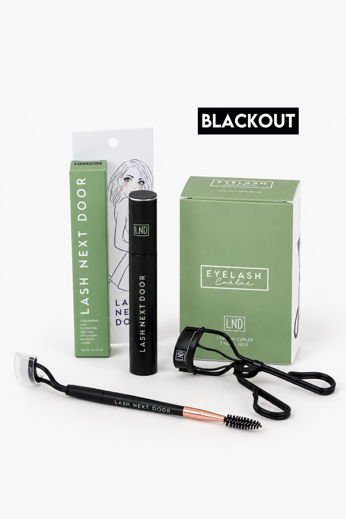 Lash Next Door eyelash extension kit in the 'Blackout' shade, featuring a black eyelash mascara tube, a green and white applicator box, a green retail box, a black eyelash curler, and a spoolie wand on a white background.