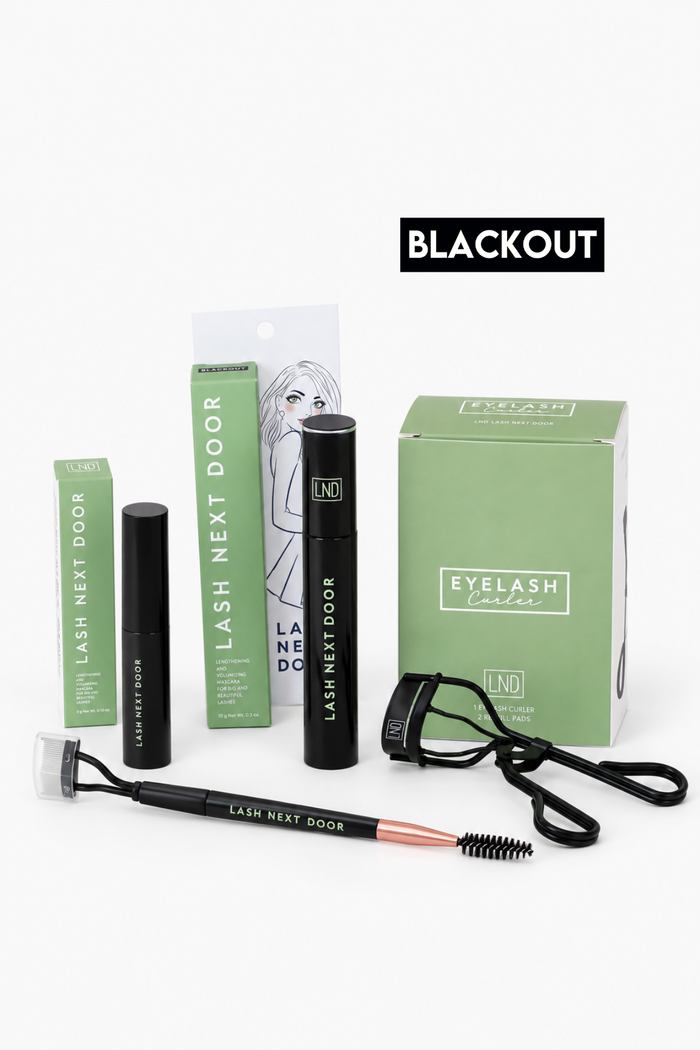 Lash Next Door eyelash extension kit in the 'Blackout' shade, featuring black mascara tubes, a black lash brush with rose gold ferrule, a black spoolie, and green packaging boxes on a white background.