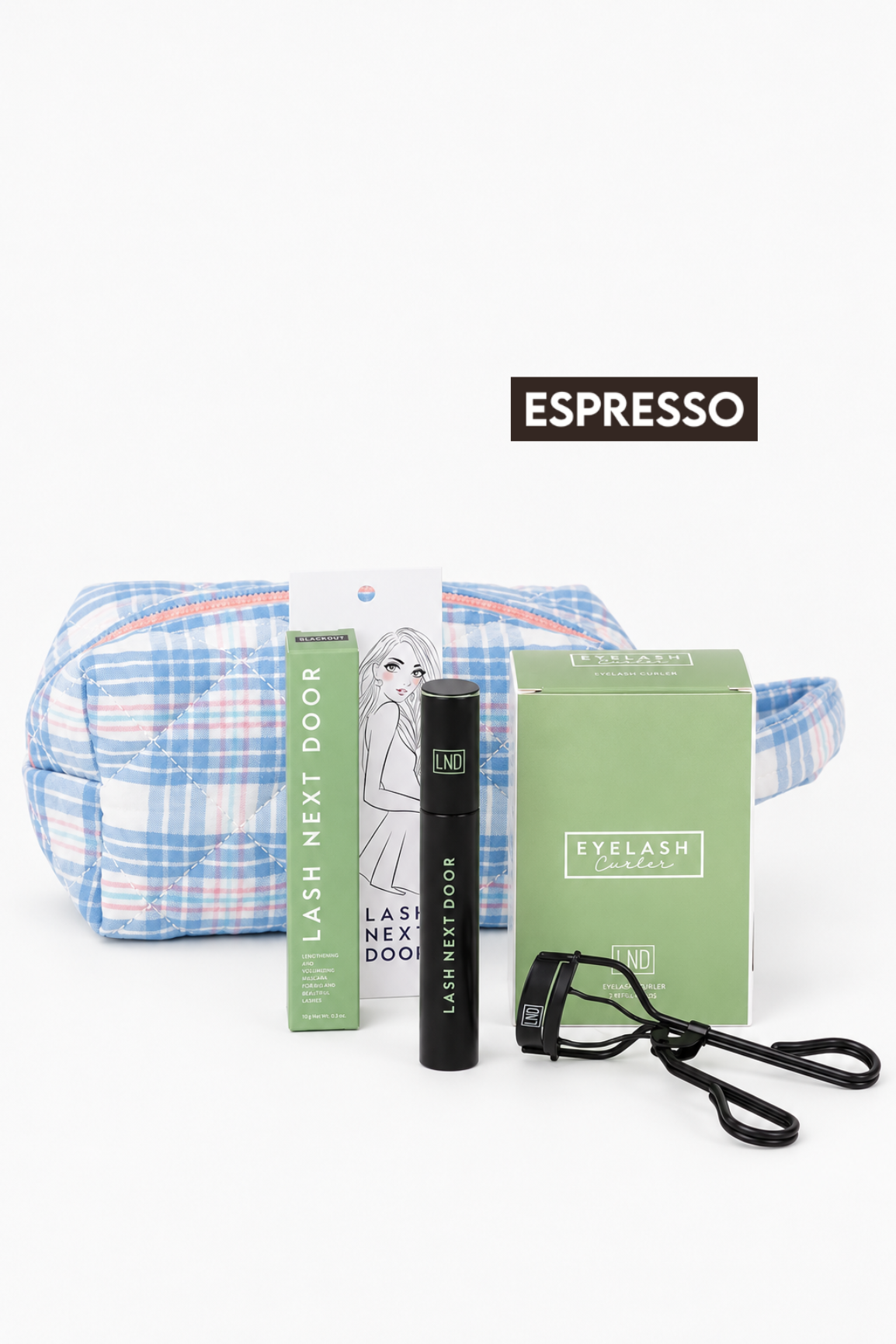 A lash care set on a white background, featuring a blue and white plaid cosmetic pouch, a green tube labeled 'LASH NEXT DOOR', a black mascara tube, a green 'EYELASH' box, and a black eyelash curler. A black label reading 'ESPRESSO' is positioned above the items.