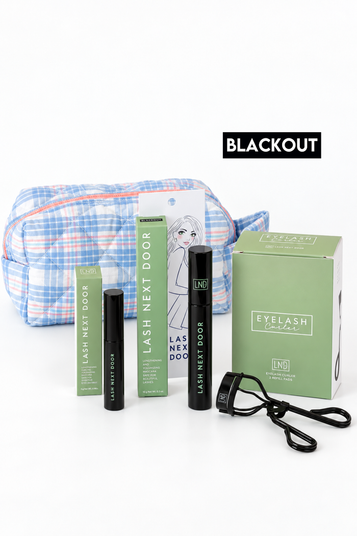 Eyelash Next Door Blackout kit featuring a blue and white plaid makeup bag, black mascara tubes, green product boxes, and a black strap, arranged on a white background with a 'BLACKOUT' label.