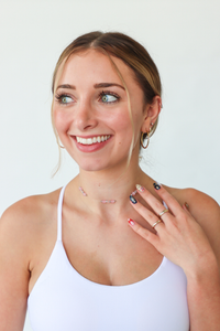 Woman wearing a white tank top with visible jewelry against a plain background