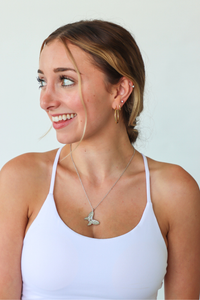 Woman wearing a white tank top and gold necklace with a butterfly pendant against a light background