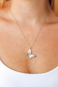 Silver butterfly necklace on a person wearing a white top