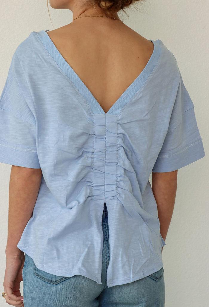 girl wearing a blue boxy t-shirt with v cut out on back and slit with ruching