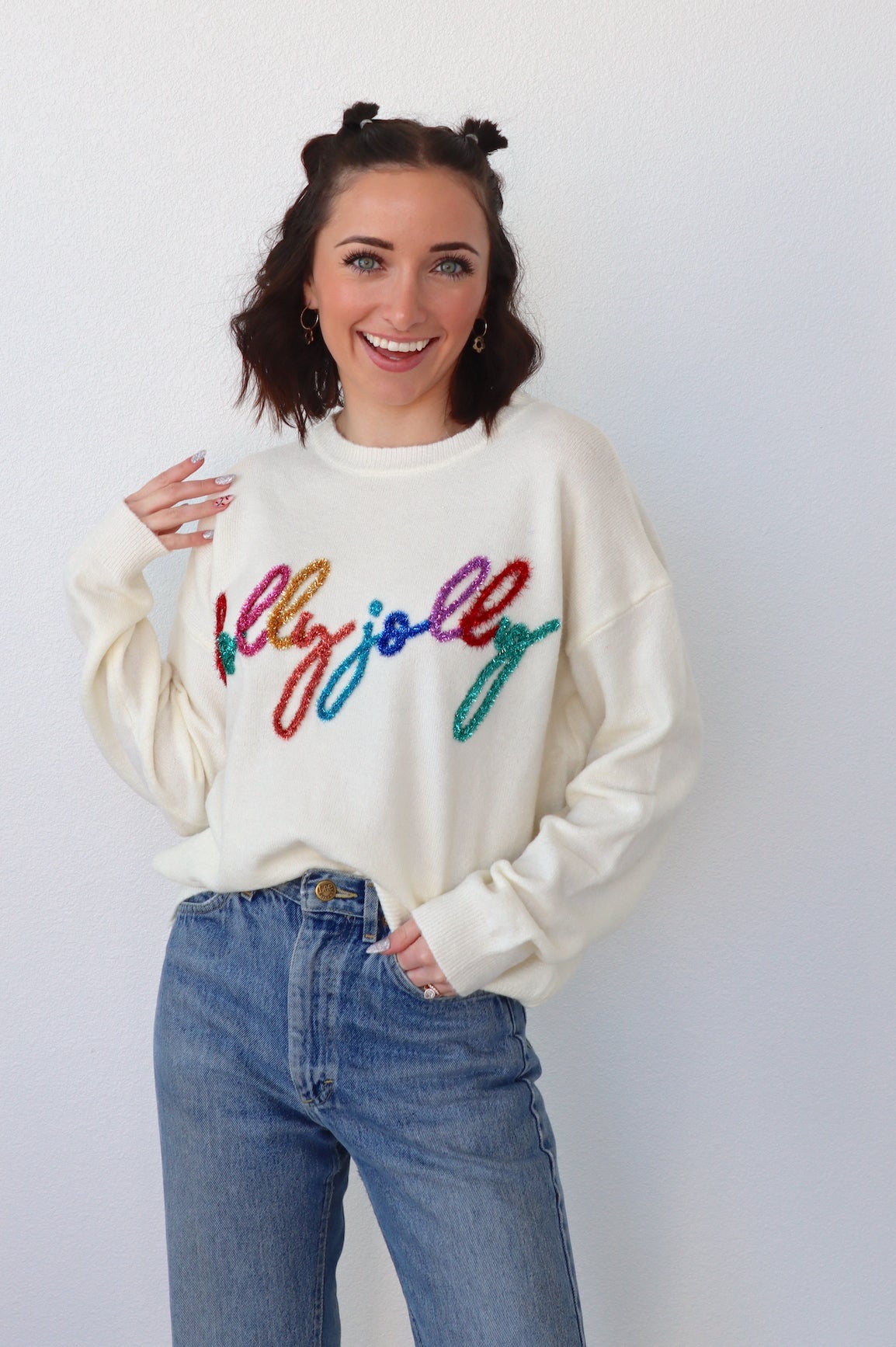 girl wearing a cream sweater that says Holly Jolly in multicolor tinsel