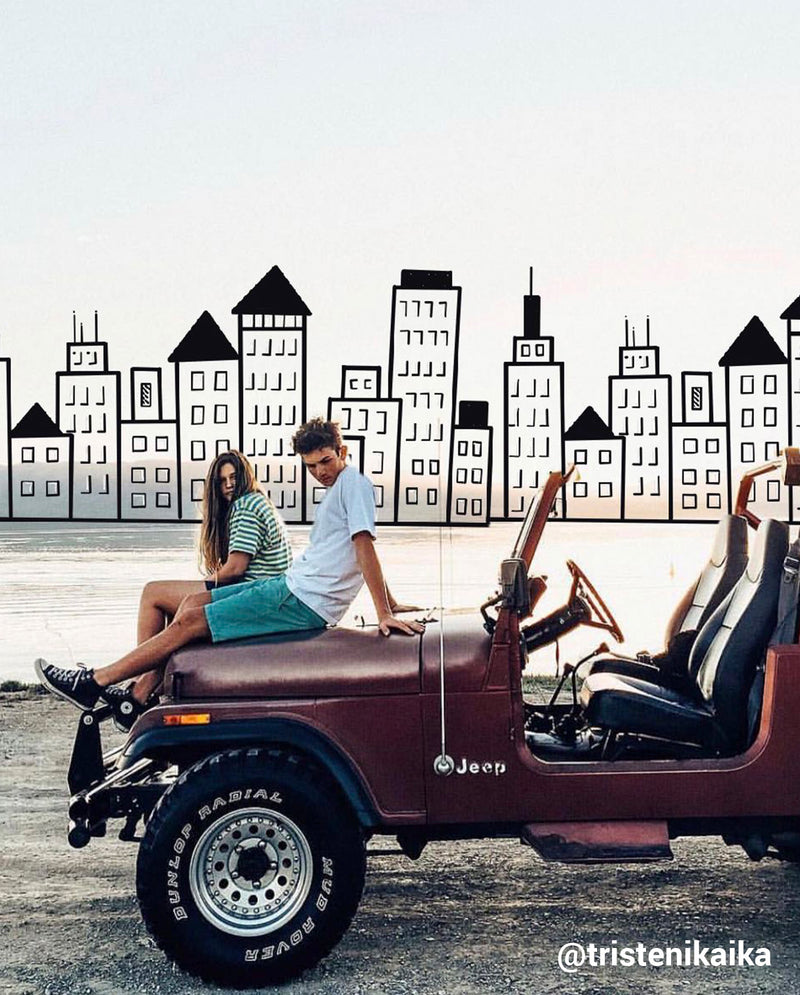 boy and girl sitting on the hood of a jeep with a drawn cityscape behind them