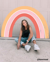 girl sitting on the floor with pink and orange rainbow drawn above her