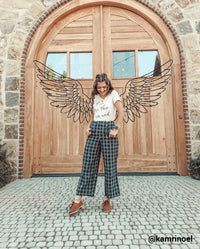girl standing in front of large wooden door with black line drawing of angel wings behind her