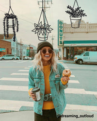 girl walking on street eating a donut and coffee with drawn hanging succulents behind her