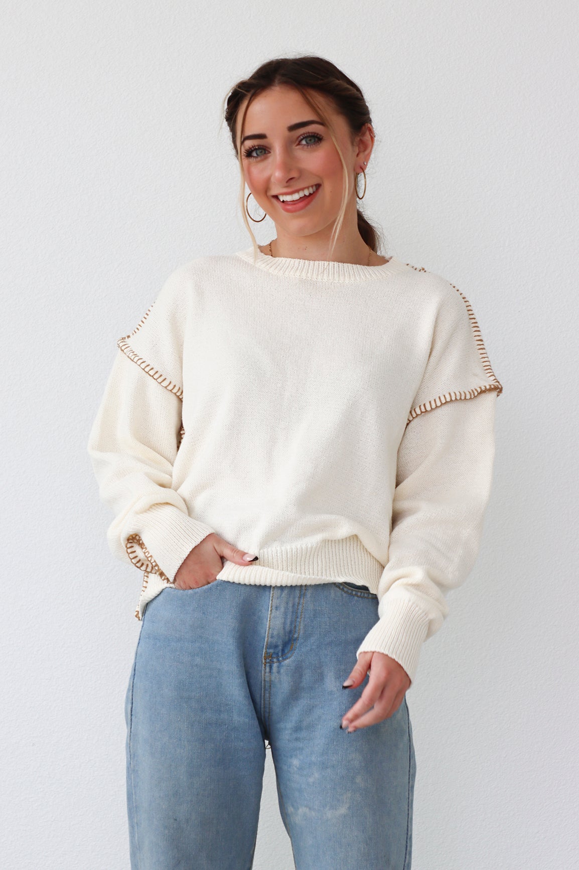 girl wearing cream sweater with brown stiching detail