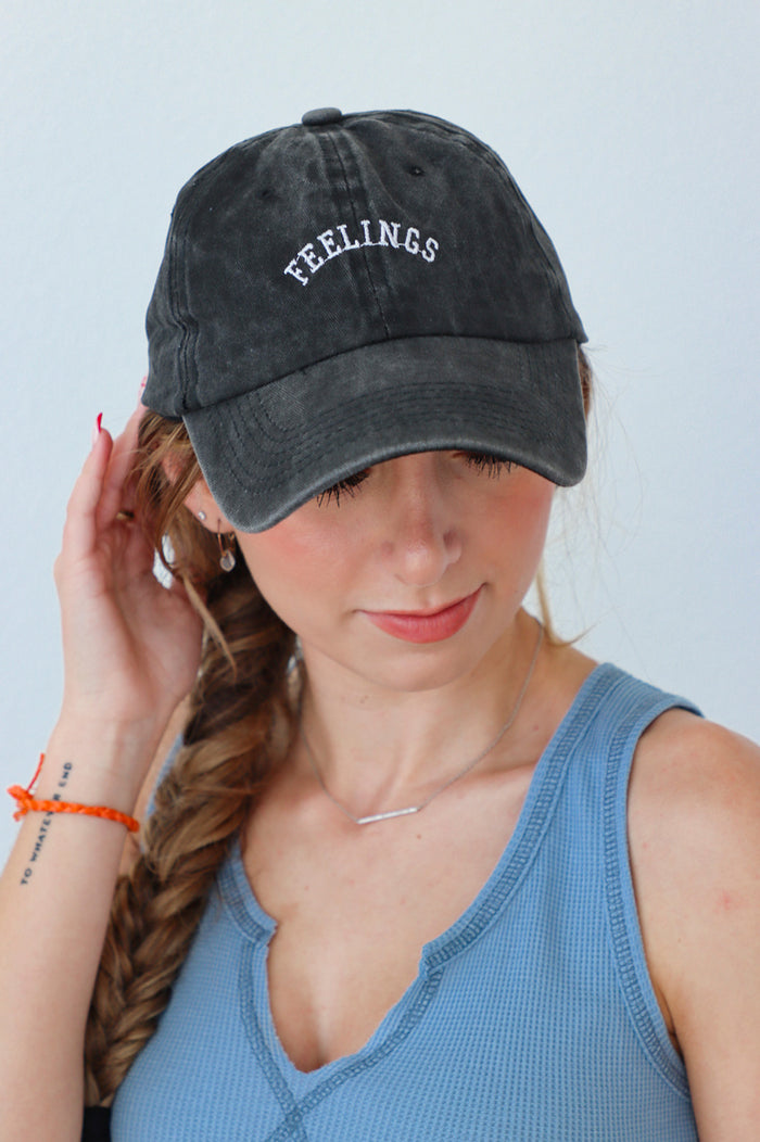 girl wearing baseball cap in charcoal with the word "feelings" stitched on to it